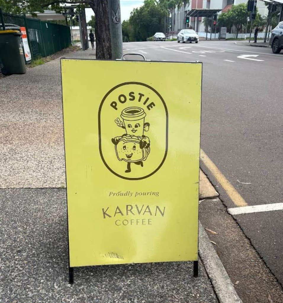 Postie A-frame sign with a coffee cup and toastie mascot, proudly pouring Karvan Coffee